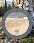 Graphite Grey Whitefish ski trail map cribbage board displayed outdoors against a pine tree in Montana.