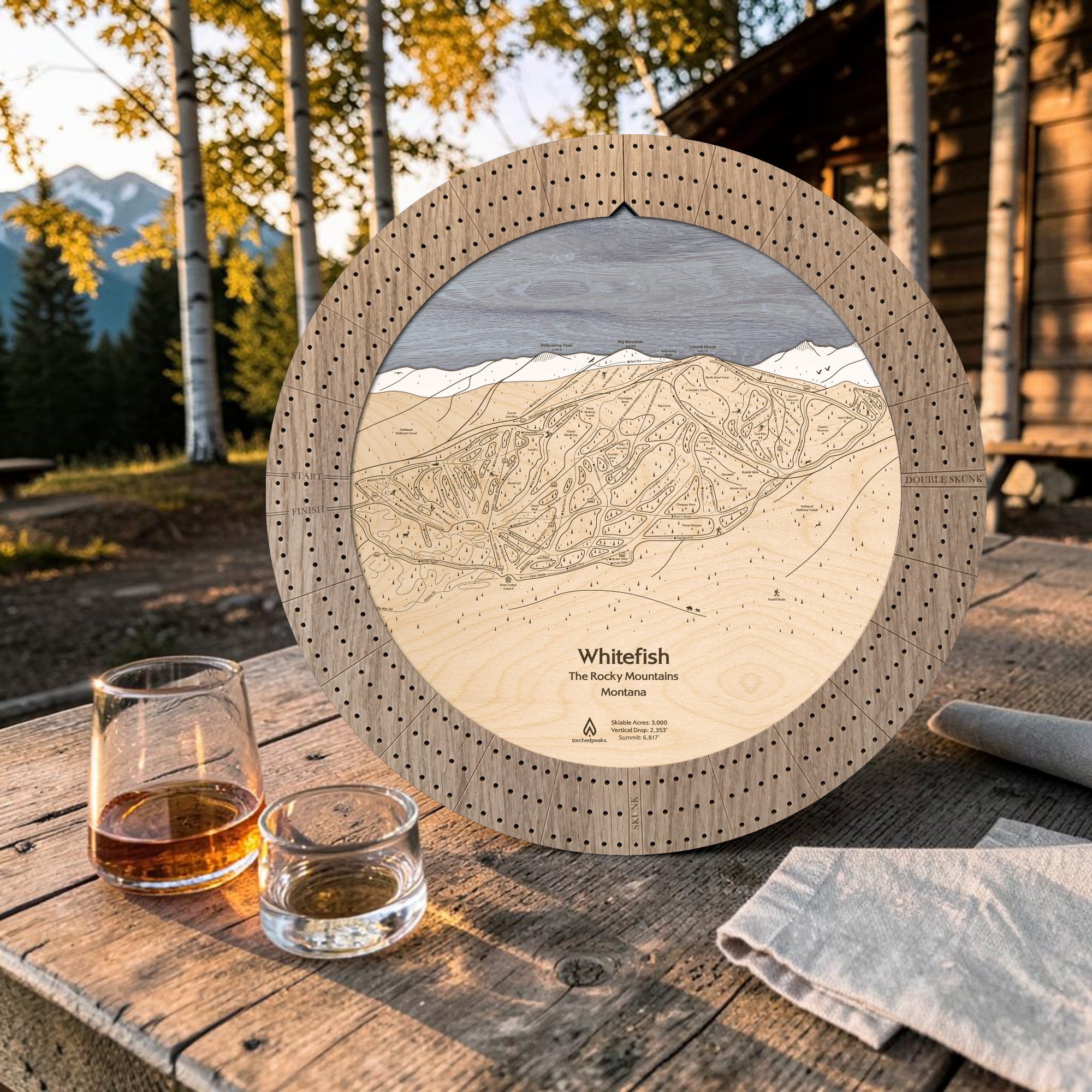 Weathered Timber Whitefish ski map cribbage board displayed outdoors with whiskey glasses for après-ski game night.