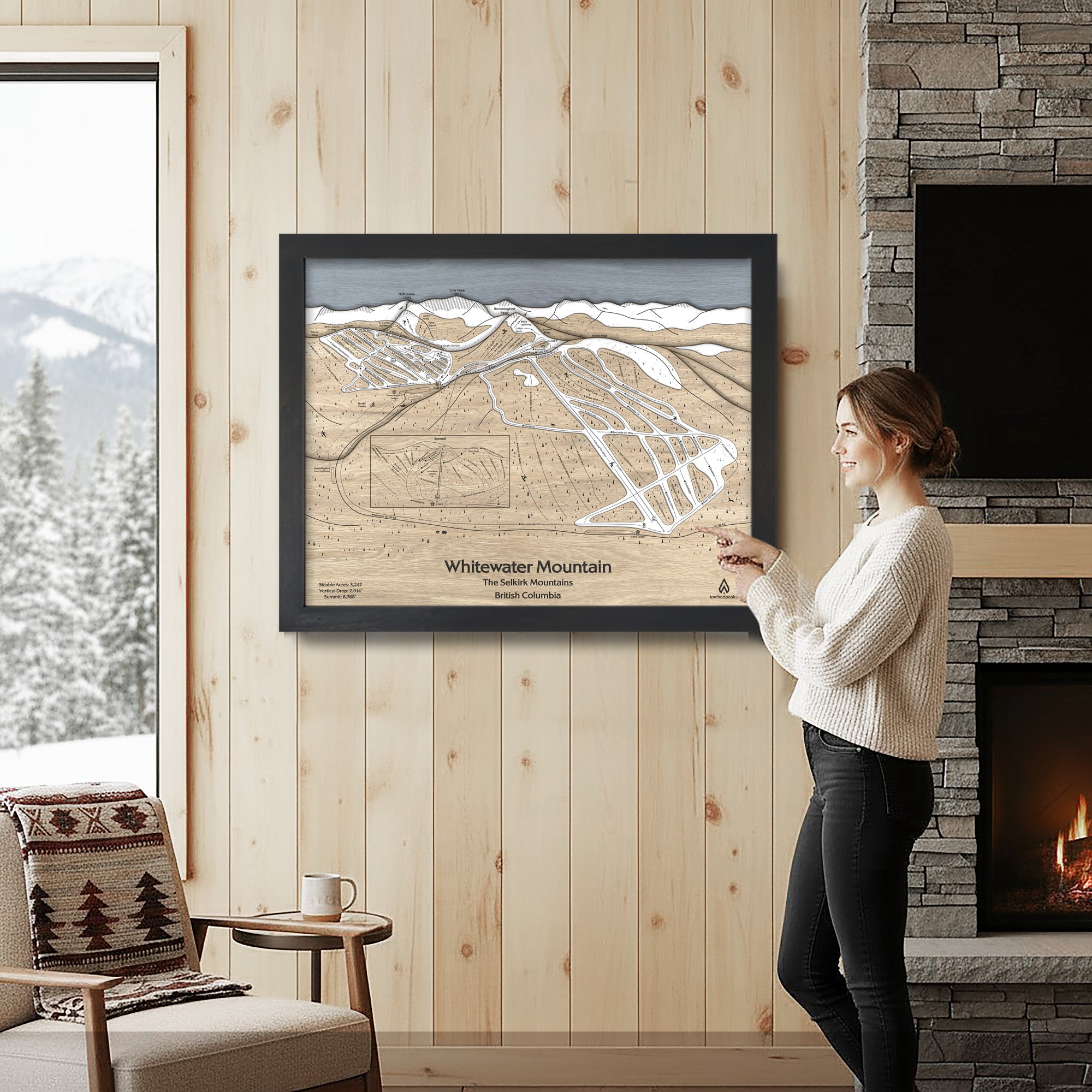 Woman standing in a cozy ski cabin with a framed map of Whitewater Mountain in British Columbia.
