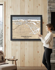 Woman standing in a cozy ski cabin with a framed map of Whitewater Mountain in British Columbia.