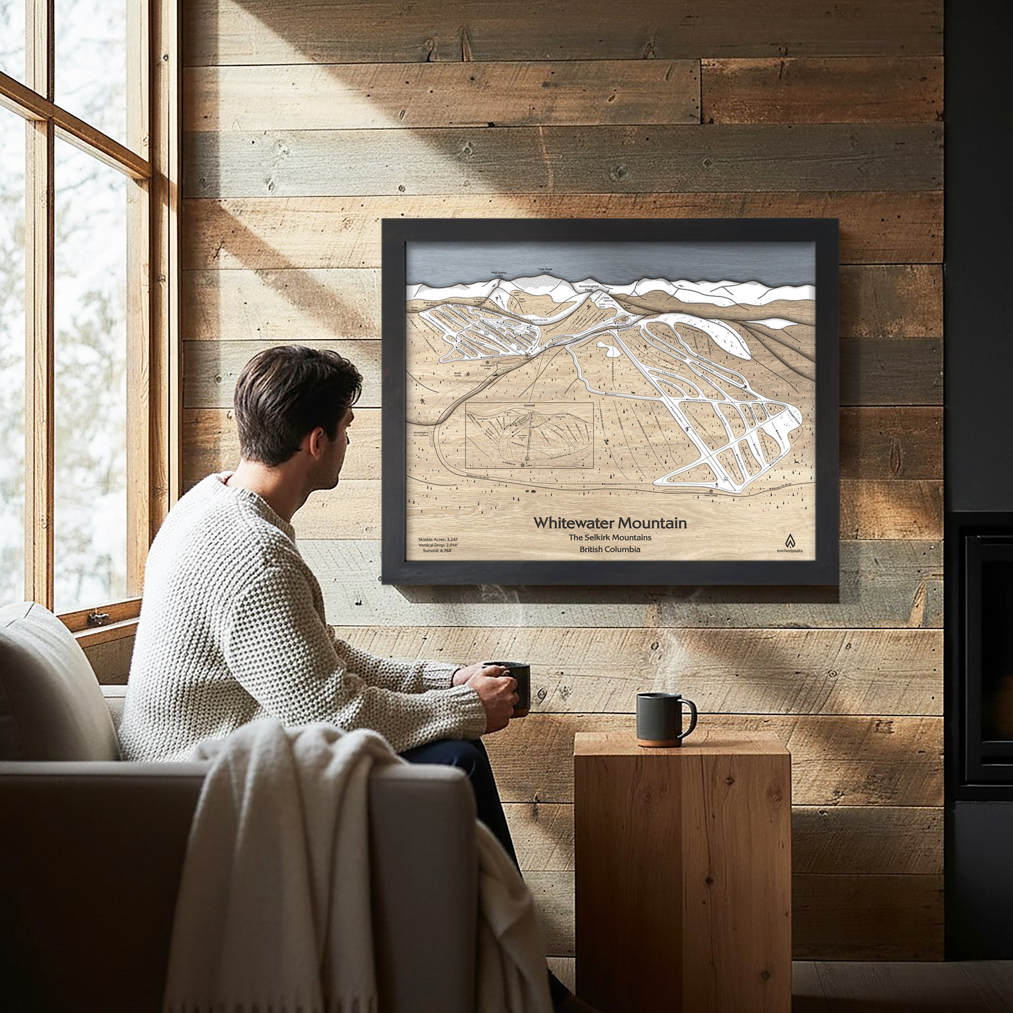 Man sitting on a couch in a cozy ski cabin with a framed map of Whitewater Mountain on the wall.