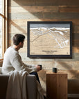 Man sitting on a couch in a cozy ski cabin with a framed map of Whitewater Mountain on the wall.