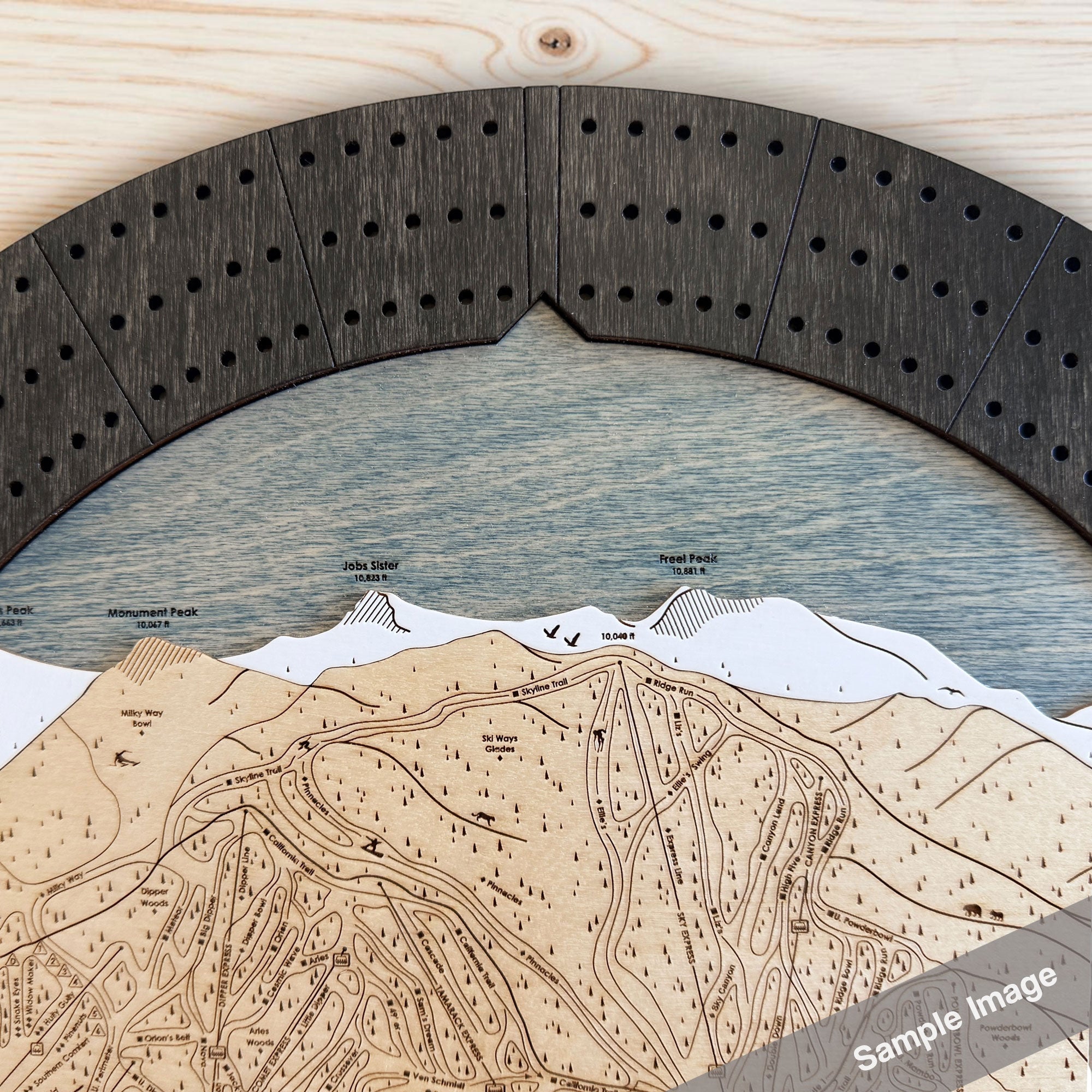 A circular wooden cribbage board game featuring a ski resort trail map in light natural wood, a birch ski slope, white snow peaks, and a matte onyx 3-player cribbage track. 