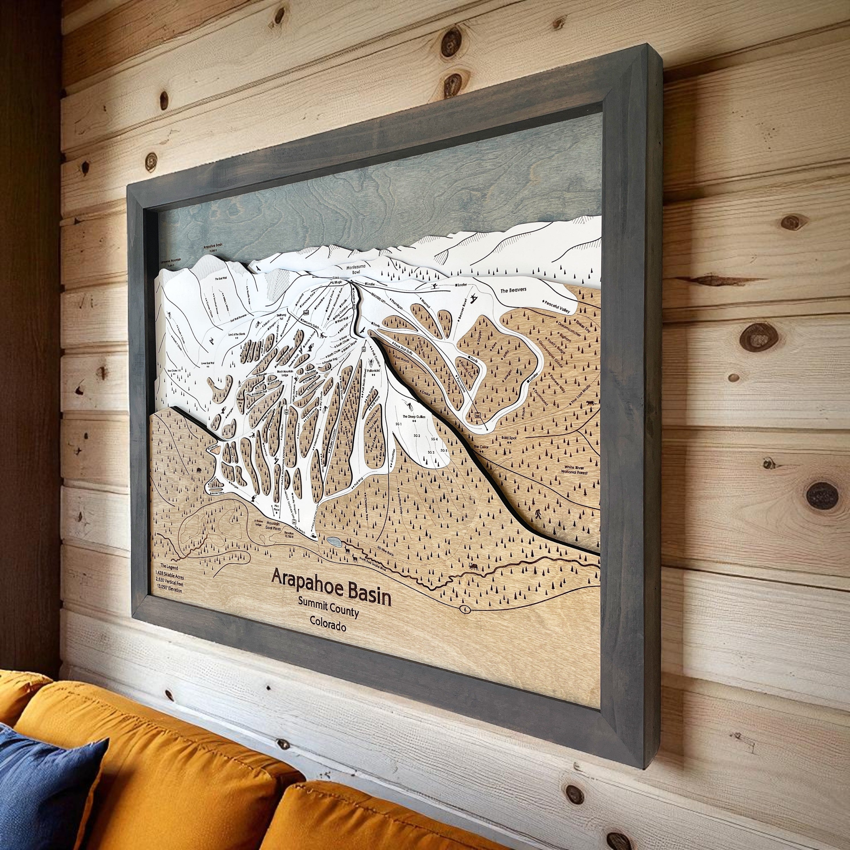 Framed topographic map of Arapahoe Basin Ski Resort on a wooden wall above a couch.