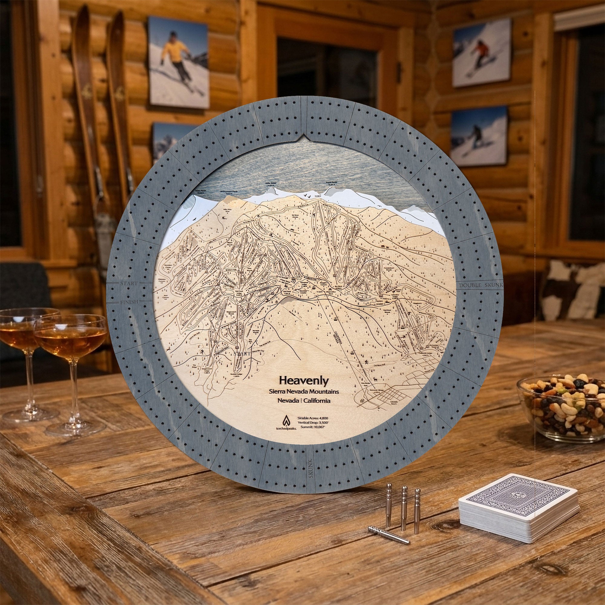 Heavenly Mountain wooden cribbage board displayed in a rustic ski cabin with playing cards, cribbage pegs, and mountain lodge décor.